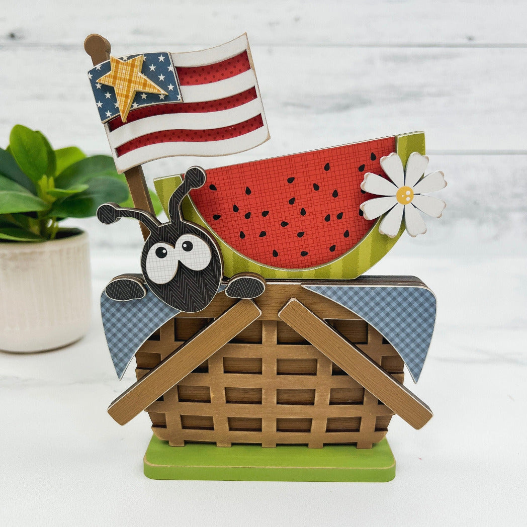 Summer ant peeking out of a picnic basket with a patriotic flag and a slice of watermelon. Summer watermelon tiered tray wood decorations. 