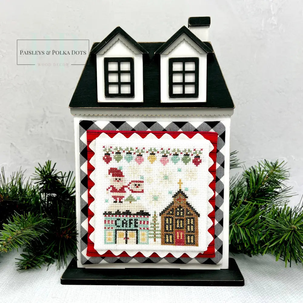 City Christmas cross stitch by Stitching with the Housewives shown on a wood city house