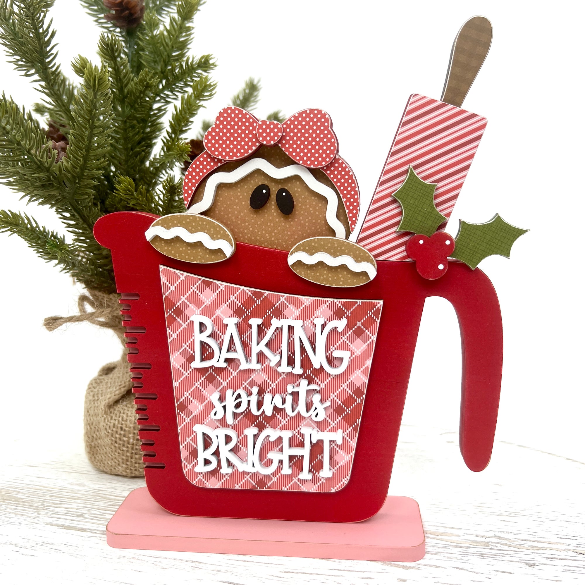Gingerbread wood decor craft kit. Measuring cup with a gingerbread girl and candy cane striped rolling pin inside. Front says Baking Spirits Bright.