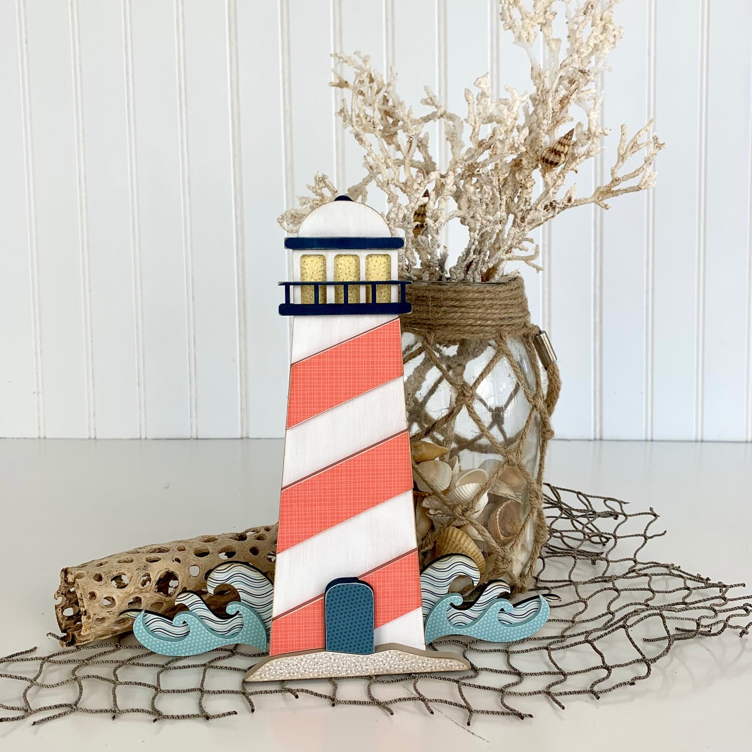 Nautical and beach themed lighthouse in blue and coral colors.  Wood lighthouse with waves and sand for styling tiered trays, shelves, and mantels. 