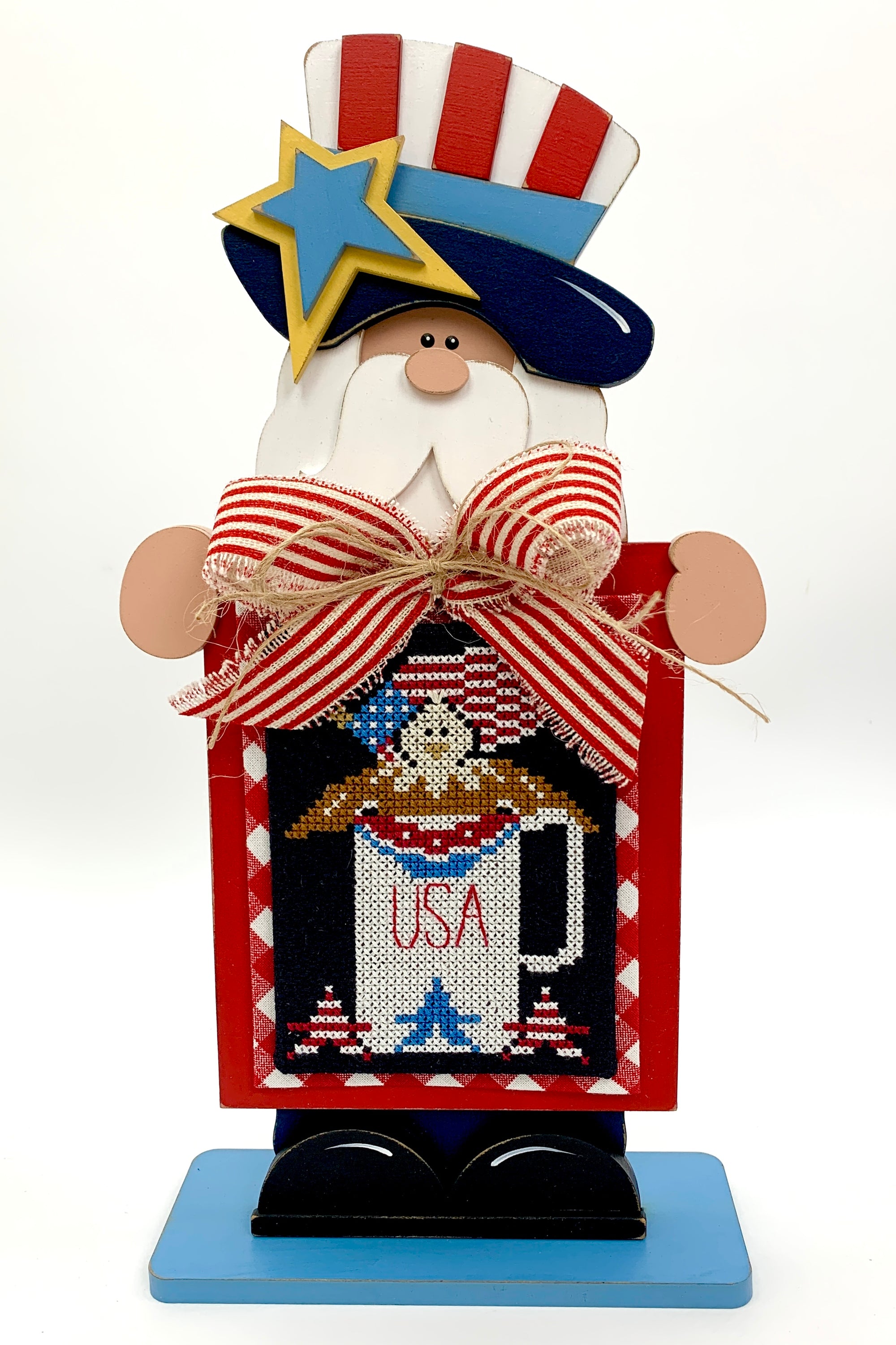 Standing Red white and blue uncle sam holding a finshed patriotic cross stitch by Stitching with the Housewives.