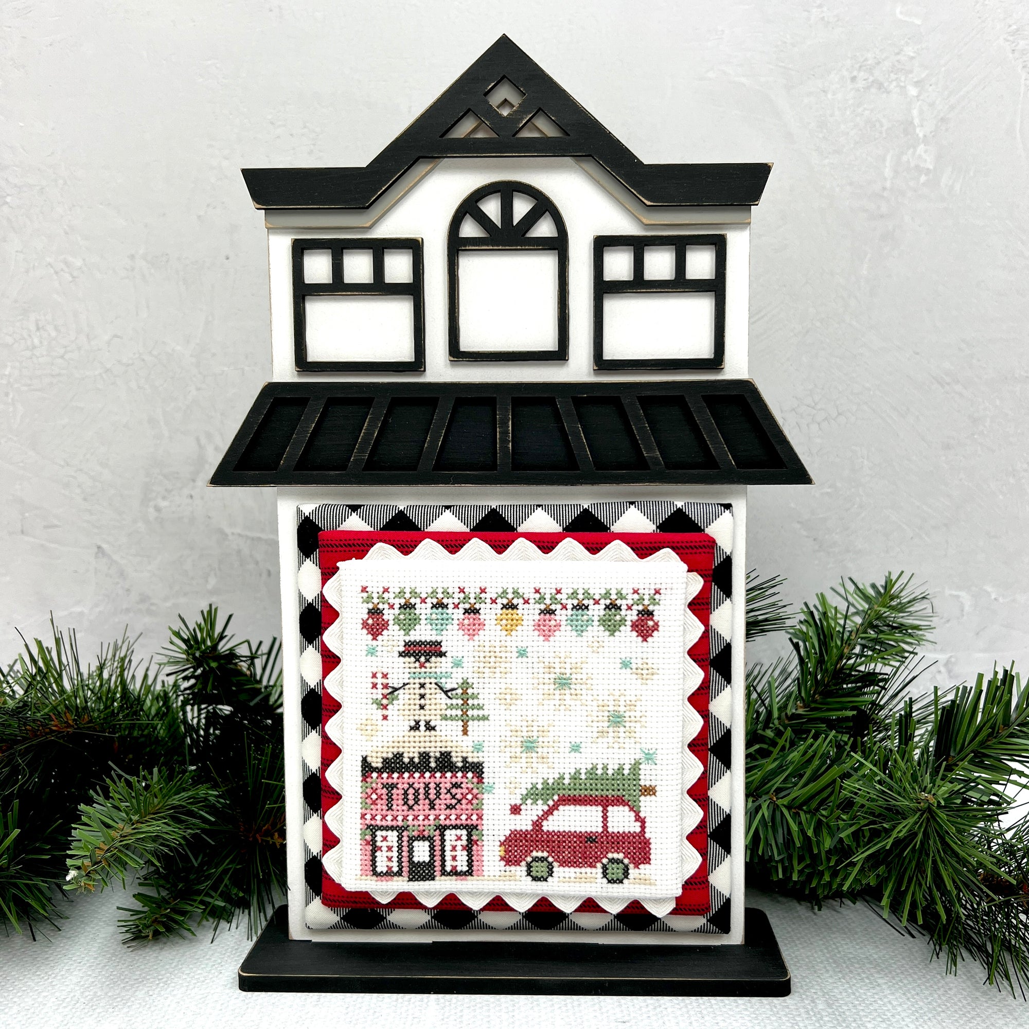City Christmas cross stitch by Stitching with the Housewives shown on a wood city house cross stitch display