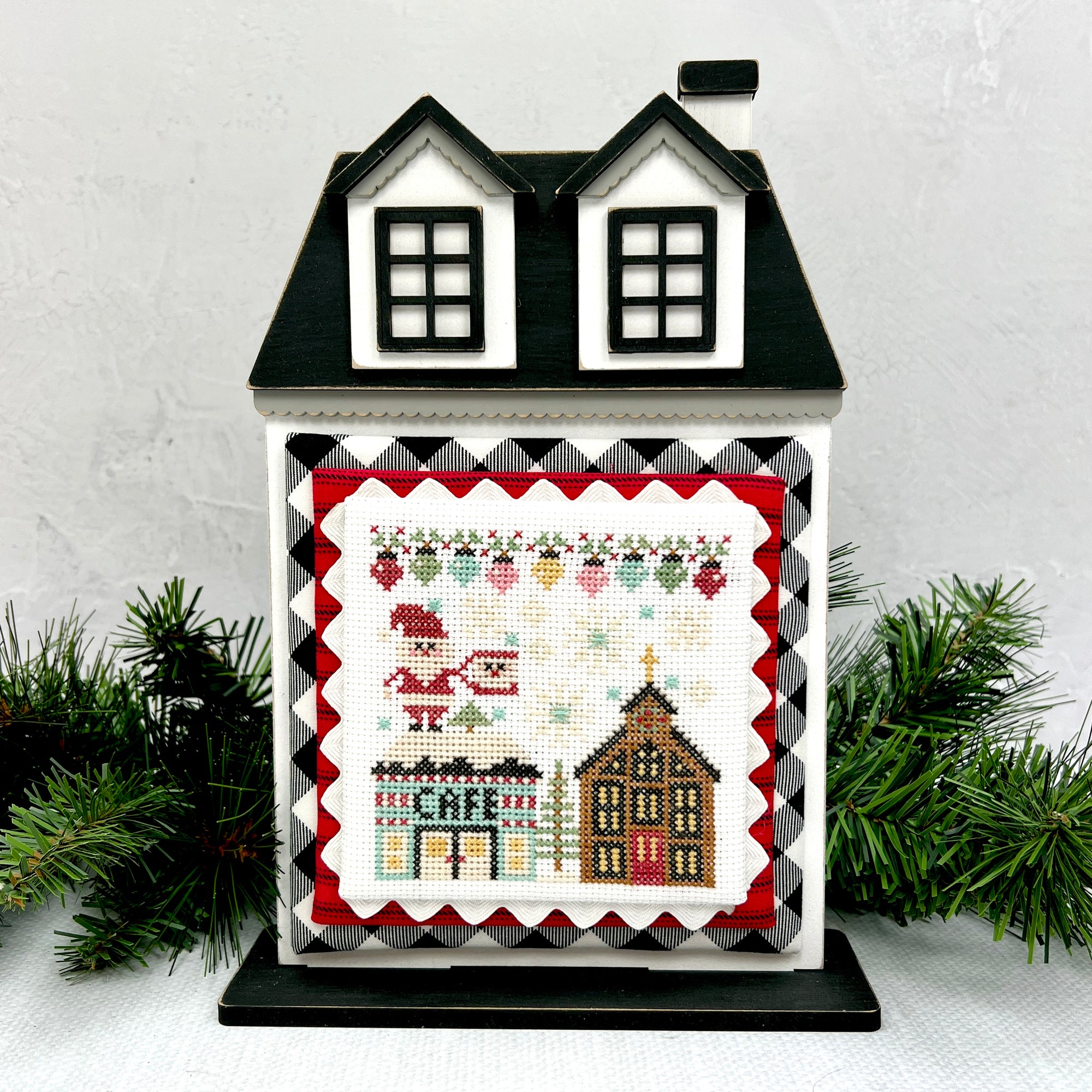 City Christmas cross stitch by Stitching with the Housewives shown on a wood city house